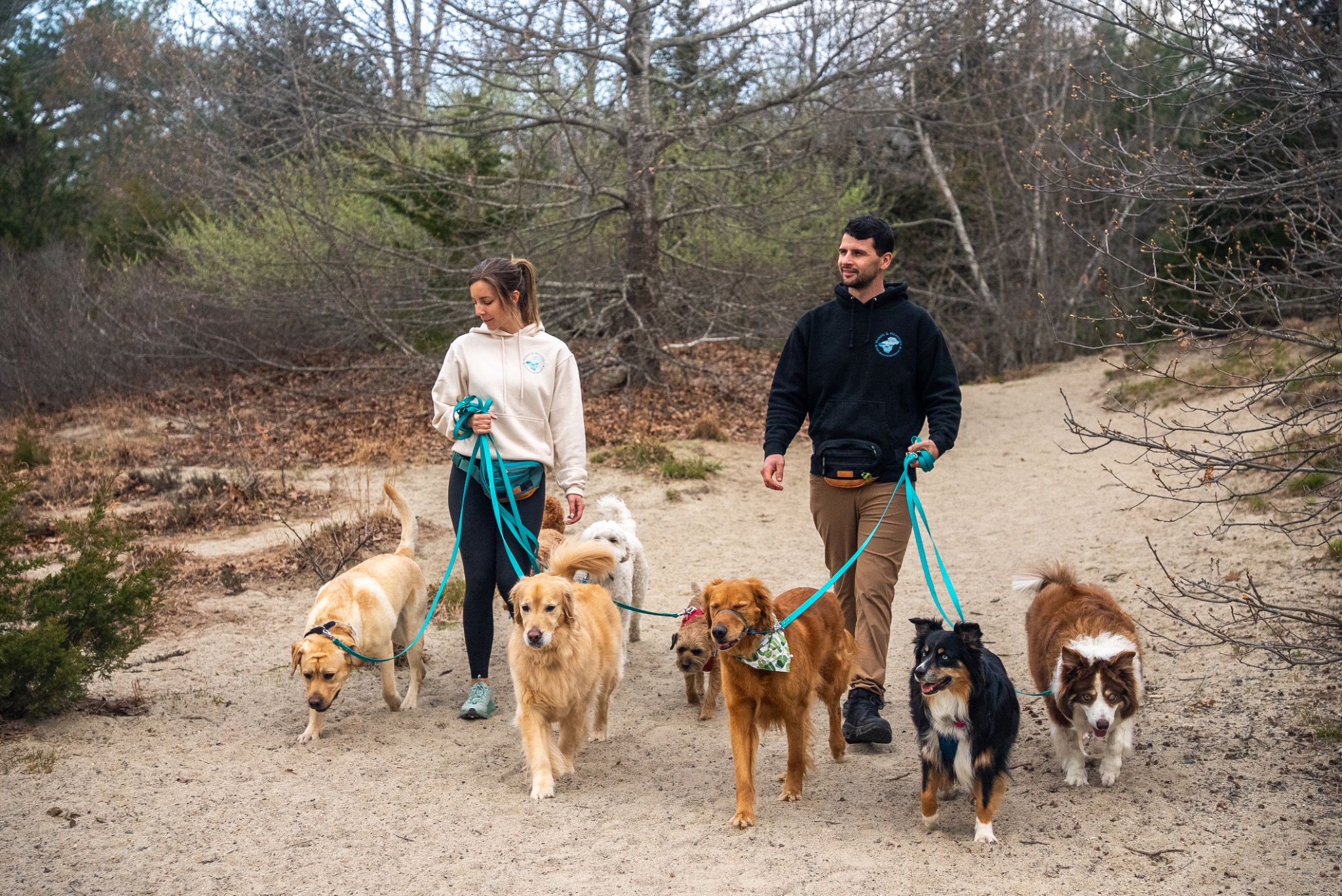 Anna and Jake walking a group of dogs together on a wooded trail